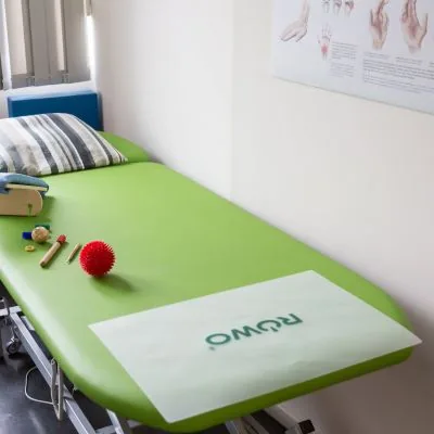 Grüne Behandlungsliege mit Therapiematerial für die Handtherapie